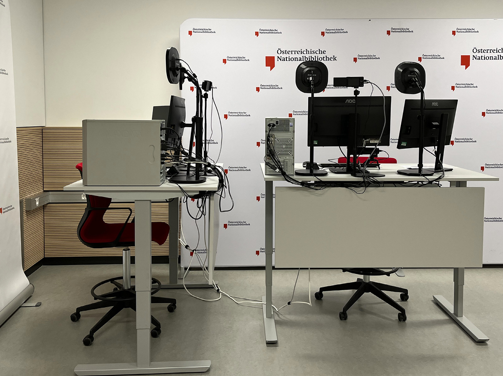 Abb. 1: Die zwei Webinararbeitsplätze mit höhenverstellbaren Tischen und Logowand im Hintergrund