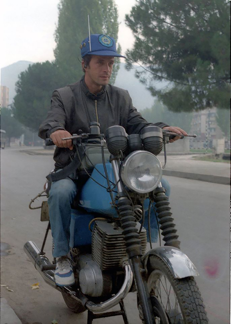 Figure 3: 
Roland Tasho, photographer of Ylli magazine in Tirana, 1988. Courtesy: private collection, Tirana. Throughout the communist period the motorcycle was an emblematic attribute of the photojournalist’s profession. At a time when private means of transport were scarce and movement across the country was limited and controlled, the motorcycle represented both relative freedom of movement and, like the camera, technological modernity that distinguished its user.