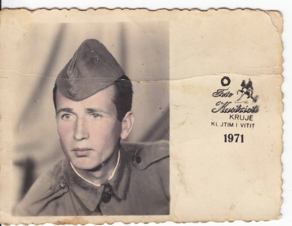 Figure 11: 
Studio portrait sent by a conscript to his family, 1971. Courtesy: Private collection, Bilisht. The picture has been colourised by the photographer or, most probably, by another employee of the public studio. The text on the right gives the name of the studio and its location, in the city of Krujë, and reads: “Souvenir from the year 1971”.